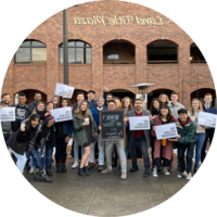 A group of students stands in a crowd holding signs promoting community service.